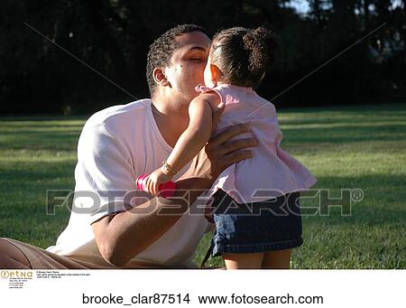 Picture - Latin father giving his daughter a kiss outside in the park.. Fotosearch