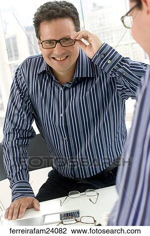 Man in his 30's smiling wearing glasses wearing a striped button down shirt looking at his reflection in a mirror. View Large Photo Image Stock Image - Man in his 30's smiling wearing glasses wearing a striped button down shirt looking at his reflection in a mirror.. Fotosearch