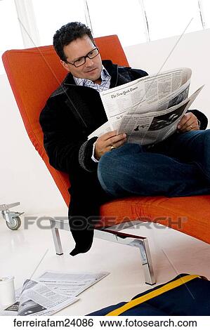 Man in his 30's wearing glasses reading a newspaper sitting on a red chair View Large Photo Image Stock Photograph - Man in his 30's wearing glasses reading a newspaper sitting on a red chair. Fotosearch