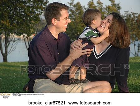 Mother and father spending time with their son outside in the park giving him hugs on the grass. View Large Photo Image Stock Image - Mother and father spending time with their son outside in the park giving him hugs on the grass. . Fotosearch
