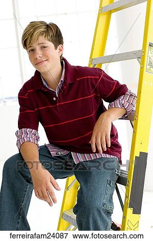 Stock Photo -  Portrait of a teenage boy sitting on a ladder in front of a window. Fotosearch
