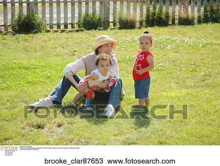 Portrait of a woman wearing a hat and her two children playing outside in the park on the grass one little girl standing. Mother and two children playing on the grass View Large Photo Image Stock Image - Portrait of a woman wearing a hat and her two children playing outside in the park on the grass one little girl standing. Mother and two children playing on the grass. Fotosearch
