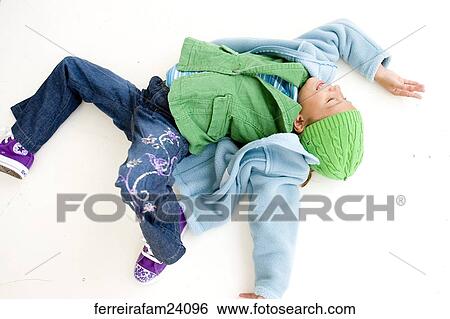 Portrait of a young girl lying on a white backdrop wearing a blue coat and green hat and purple sneakers. View Large Photo Image Stock Photograph - Portrait of a young girl lying on a white backdrop wearing a blue coat and green hat and purple sneakers.. Fotosearch
