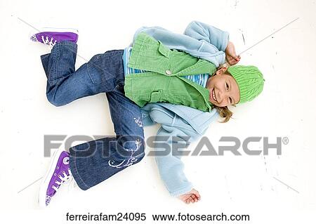 Portrait of a young girl lying on a white backdrop wearing a blue coat and green hat and purple sneakers. View Large Photo Image Stock Photography - Portrait of a young girl lying on a white backdrop wearing a blue coat and green hat and purple sneakers.. Fotosearch