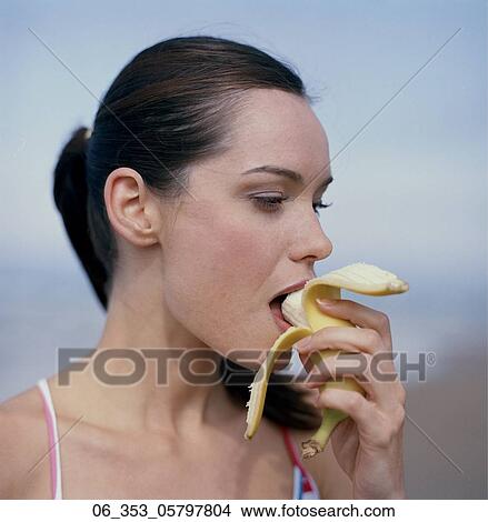 Picture - Side view of woman on a beach eating a bananana. Fotosearch