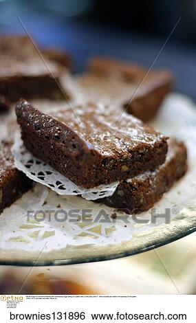 Still life image of a brownie powdered with confectionary sugar sitting on a platter with a white doily under it. Other brownies are visible in the backdrop on the platter. View Large Photo Image Stock Photograph - Still life image of a brownie powdered with confectionary sugar sitting on a platter with a white doily under it. Other brownies are visible in the backdrop on the platter.. Fotosearch
