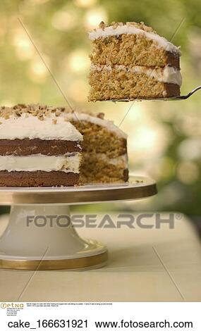 Still life image of a cake with white frosting and topped with nuts sitting on a platter. A slice of cake is being cut and removed. View Large Photo Image Stock Image - Still life image of a cake with white frosting and topped with nuts sitting on a platter. A slice of cake is being cut and removed.. Fotosearch