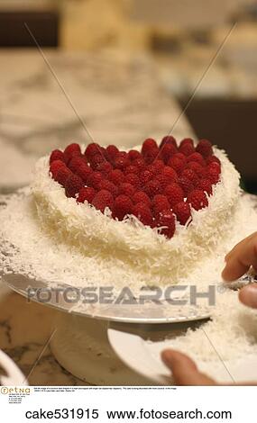 Still life image of a coconut cake shaped in a heart and topped with bright red raspberries/ raspberry. The cake is being decorated with more coconut in the image. View Large Photo Image Stock Photography - Still life image of a coconut cake shaped in a heart and topped with bright red raspberries/ raspberry. The cake is being decorated with more coconut in the image.. Fotosearch
