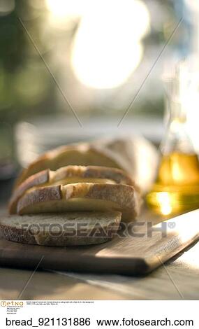 Stock Photograph -  Still life image of a sliced loaf of bread sitting on a cutting board with a flask of oil in the background.. Fotosearch