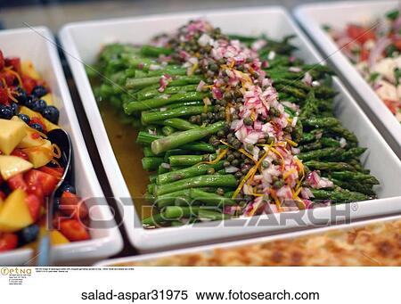 Stock Photography -  Still life image of asparagus salad with chopped garnishes spread on top. Other foods and salads are vivible.. Fotosearch