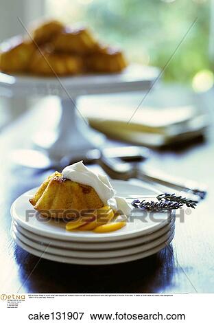 Still life indoor image of a mini small cake topped with whipped cream and with sliced peaches and some plant garnishes to the side of the cake. A platter of small cakes are visible in the background. View Large Photo Image Stock Photo - Still life indoor image of a mini small cake topped with whipped cream and with sliced peaches and some plant garnishes to the side of the cake. A platter of small cakes are visible in the background.. Fotosearch