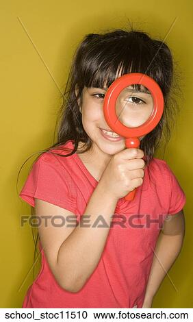 Stock Image -  Stock images of science related topics Girl Student peers through a magnifying glass. she's wearing a pink shirt and has her hair pulled into pigtails.. Fotosearch