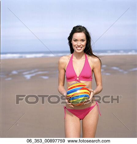 SummeBeauty Woman standing on a beach wearing a pink halterneck bikini holding a spiral coloure View Large Photo Image Stock Photo - SummeBeauty Woman standing on a beach wearing a pink halterneck bikini holding a spiral coloure. Fotosearch