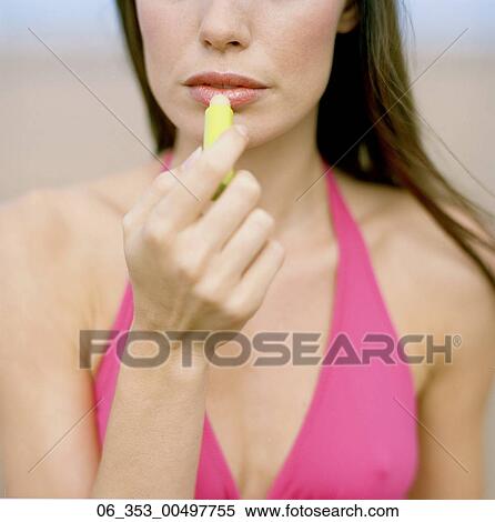 Stock Photography - Summer BeautyCropped image of woman wearing a pink halterneck bikini applying lip salve to her lips . Fotosearch