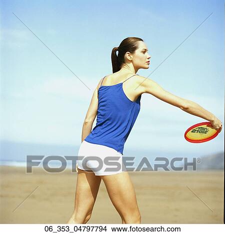 Summer BeautySide view of a woman standing on a beach wearing a blue vest top throwing a red and yellowbee View Large Photo Image Picture - Summer BeautySide view of a woman standing on a beach wearing a blue vest top throwing a red and yellowbee. Fotosearch