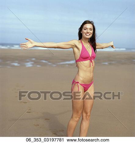 Stock Image - Summer BeautyWoman standing on a beach wearing a pink halterneck bikini arms outstretched . Fotosearch