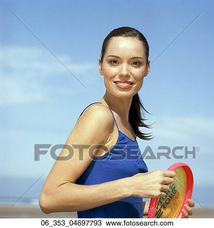 Summer BeautyWoman standing on a beach wearing a blue vest top holding red and yellow frisbee View Large Photo Image Stock Image - Summer BeautyWoman standing on a beach wearing a blue vest top holding red and yellow frisbee . Fotosearch