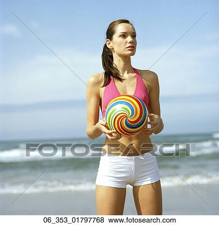 Summer BeautyWoman standing on a beach wearing a pink halterneck bikini top and white shorts holding a spiral coloured ball View Large Photo Image Stock Photo - Summer BeautyWoman standing on a beach wearing a pink halterneck bikini top and white shorts holding a spiral coloured ball . Fotosearch