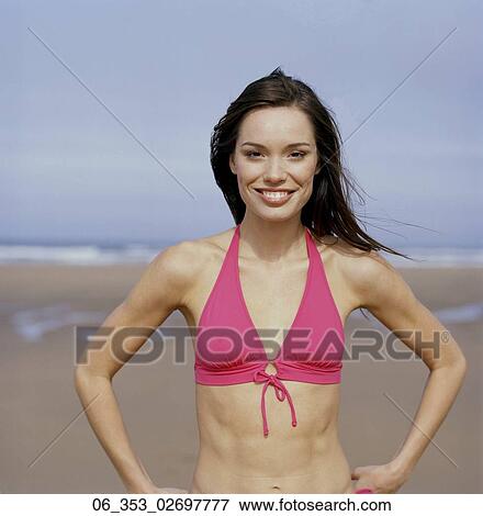 Stock Photo - Summer BeautyWoman standing on a beach wearing a pink halterneck bikini with her hands on her hips . Fotosearch