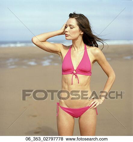 Summer BeautyWoman standing on a beach wearing a pink halterneck bikini with one hand on her hip and the other touching the side of her face View Large Photo Image Stock Photo - Summer BeautyWoman standing on a beach wearing a pink halterneck bikini with one hand on her hip and the other touching the side of her face. Fotosearch