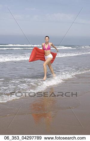 Summer BeautyWoman wearing a pink halterneck bikini and white hotpants shorts running on the beach holding a red lilo View Large Photo Image Stock Photo - Summer BeautyWoman wearing a pink halterneck bikini and white hotpants shorts running on the beach holding a red lilo . Fotosearch