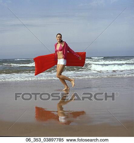 Summer BeautyWoman wearing a pink halterneck bikini white hotpants shorts and cardigan running on the beach holding a red lilo " View Large Photo Image Stock Photography - Summer BeautyWoman wearing a pink halterneck bikini white hotpants shorts and cardigan running on the beach holding a red lilo ". Fotosearch