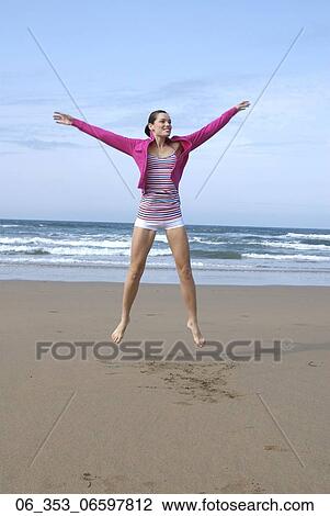 Stock Image - Summer Woman Woman jumping on a beach wearing a stripey vest top white hotpant shorts pink cardigan with arms outstretch". Fotosearch