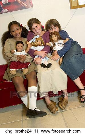 Stock Image -  Three young girls sitting down holding dolls. Fotosearch