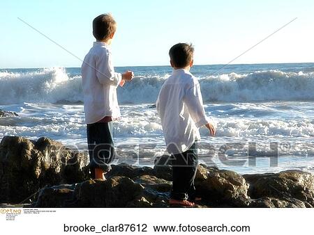 Two boys standing outside on some rocks near water View Large Photo Image Stock Image - Two boys standing outside on some rocks near water. Fotosearch