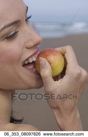 Stock Photograph - Woman BeachCropped image of a woman on a beach eating an apple . Fotosearch