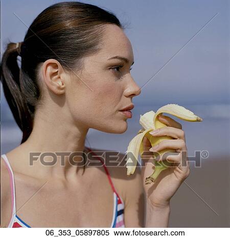 Stock Photography - Woman BeachSide view of woman wearing stripey vest top on a beach eating a banana . Fotosearch