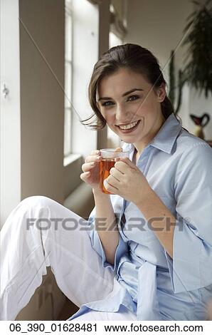 Woman DrinkingWoman wearing a blue shirt and white trousers holding a glass mug View Large Photo Image Stock Image - Woman DrinkingWoman wearing a blue shirt and white trousers holding a glass mug . Fotosearch