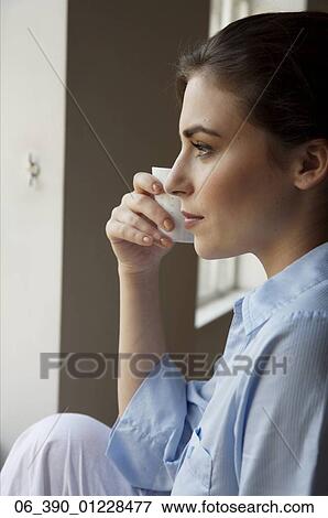 Woman DrinkingWoman wearing a blue shirt holding a white cup whilst staring out of the window View Large Photo Image Stock Photo - Woman DrinkingWoman wearing a blue shirt holding a white cup whilst staring out of the window . Fotosearch