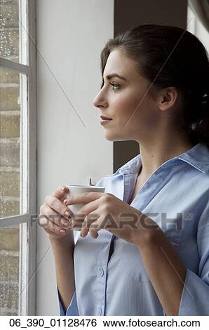 Woman DrinkingWoman wearing a blue shirt holding a white cup whilst staring out of the window View Large Photo Image Stock Photograph - Woman DrinkingWoman wearing a blue shirt holding a white cup whilst staring out of the window . Fotosearch