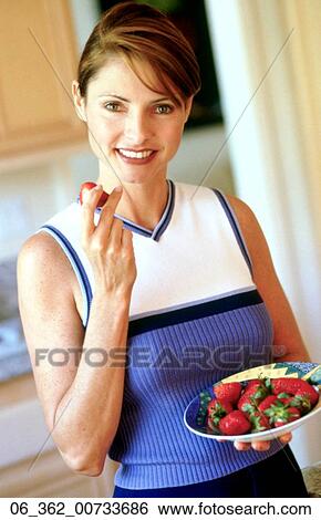 Stock Photograph -  Woman eatingWoman holding a bowl of strawberries in one hand and a strawberry in another . Fotosearch