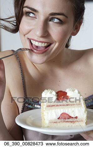 Stock Image -  Woman FoodClose up of a woman wearing strappy taupe top reclining on a sofa eating a slice of fresh cream and strawberry gateau . Fotosearch