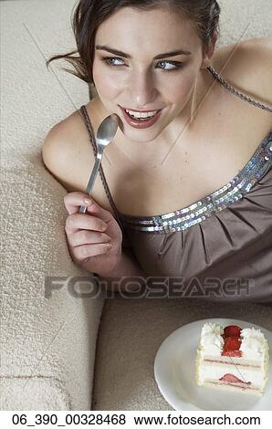 Woman FoodWoman wearing strappy taupe top reclining on a sofa eating a slice of fresh cream and strawberry gateau View Large Photo Image Stock Photo - Woman FoodWoman wearing strappy taupe top reclining on a sofa eating a slice of fresh cream and strawberry gateau . Fotosearch