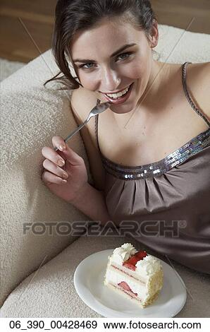 Woman FoodWoman wearing strappy taupe top reclining on a sofa eating a slice of fresh cream and strawberry gateau View Large Photo Image Stock Photo - Woman FoodWoman wearing strappy taupe top reclining on a sofa eating a slice of fresh cream and strawberry gateau . Fotosearch