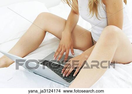 Picture -  Woman sitting in bed using a laptop computer. Fotosearch