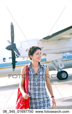Stock Image - Woman TravellingWoman holding a red bag walking away from a small aircraft . Fotosearch