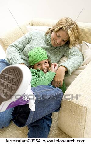 Woman wering a green sweater and a young girl wearing a green hat and a green jacket sitting in a chair. The girl leans agains the woman. View Large Photo Image Picture - Woman wering a green sweater and a young girl wearing a green hat and a green jacket sitting in a chair. The girl leans agains the woman. . Fotosearch