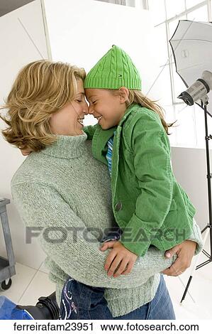 Stock Image -  Woman wering a green sweater and a young girl wearing a green hat and a green jacket. The woman holds the girl.. Fotosearch