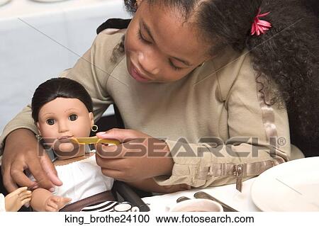 Stock Image -  Young African American girl feeding her doll.. Fotosearch