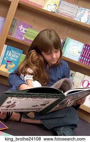 Stock Photo -  Young girl sitting on the floor cross legged holding a doll and reading a book. Fotosearch