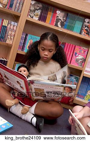 Young girl sitting on the floor cross legged holding a doll and reading a book. View Large Photo Image Stock Photo - Young girl sitting on the floor cross legged holding a doll and reading a book.. Fotosearch