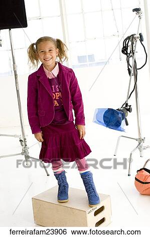 Stock Photograph -  Young girl wearing a burgundy skirt outfit and blue boots in front of a white back drop standing on a box. . Fotosearch