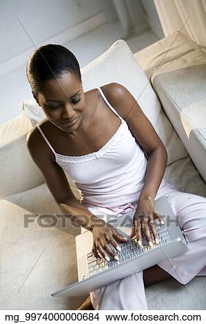 Picture - A young african american woman working on her laptop in her pajamas.. Fotosearch