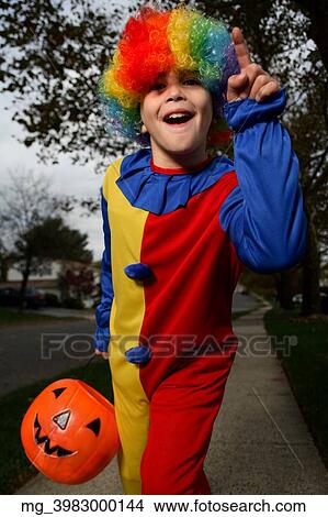 A young boy on the sidewalk on the quest for more halloween candy. He is dressed in a yellow, red and blue clown costume accompanied with a rainbow wig. He is holding a pumpkin filled with candy. © Retna Digital / Retna Ltd. View Large Photo Image Picture - A young boy on the sidewalk on the quest for more halloween candy. He is dressed in a yellow, red and blue clown costume accompanied with a rainbow wig. He is holding a pumpkin filled with candy. © Retna Digital / Retna Ltd.. Fotosearch