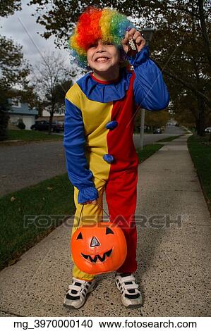 A young boy on the sidewalk on the quest for more halloween candy. He is dressed in a yellow, red and blue clown costume accompanied with a rainbow wig. He is holding a pumpkin filled with candy. © Retna Digital / Retna Ltd. View Large Photo Image Stock Image - A young boy on the sidewalk on the quest for more halloween candy. He is dressed in a yellow, red and blue clown costume accompanied with a rainbow wig. He is holding a pumpkin filled with candy. © Retna Digital / Retna Ltd.. Fotosearch