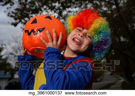 A young boy on the sidewalk on the quest for more halloween candy. He is dressed in a yellow, red and blue clown costume accompanied with a rainbow wig. He is holding a pumpkin filled with candy. © Retna Digital / Retna Ltd. View Large Photo Image Stock Photo - A young boy on the sidewalk on the quest for more halloween candy. He is dressed in a yellow, red and blue clown costume accompanied with a rainbow wig. He is holding a pumpkin filled with candy. © Retna Digital / Retna Ltd.. Fotosearch